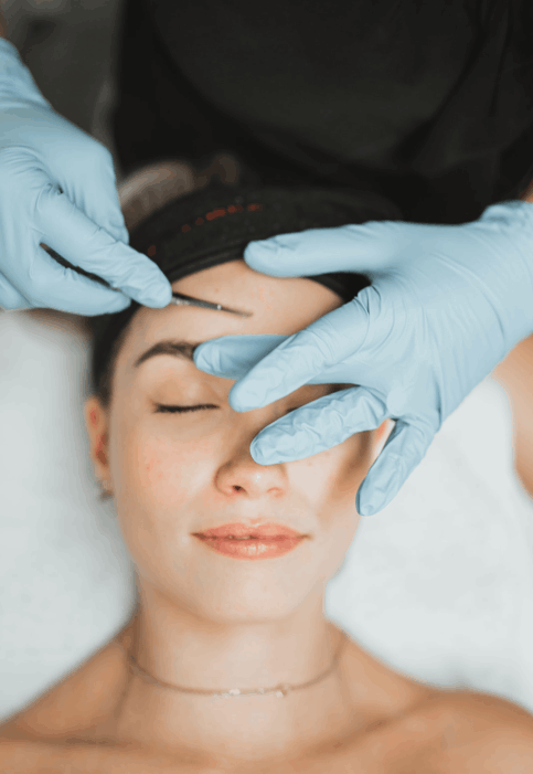 A professional in light blue gloves using a sterile surgical blade to perform a dermaplaning exfoliation treatment on a client's forehead